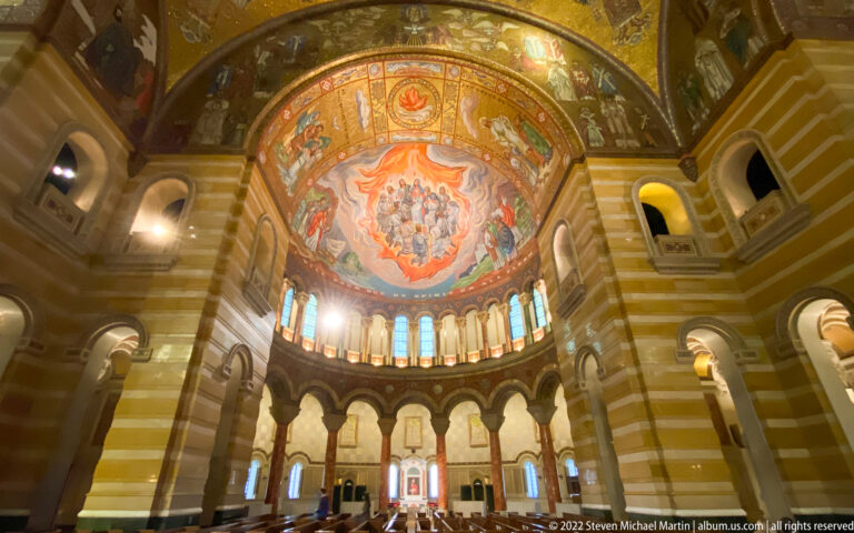 A large figural mosaic fills the apse above colored windows and the centered sanctuary.