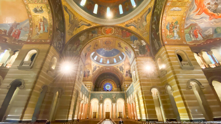 Nested mosaic arches and blue windows lead above the nave toward the cathedral sanctuary.