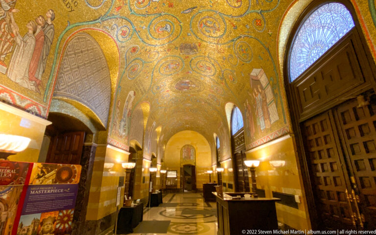 A gold mosaic vault spans an entrance hall with wooden doors, arched windows, and patterned flooring.