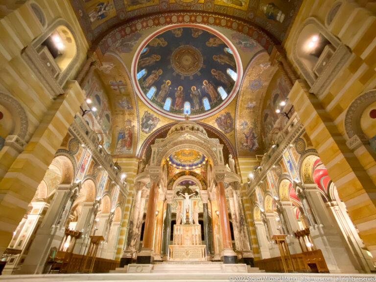 Pews and columns flank the central aisle leading to the high altar beneath a mosaic dome.
