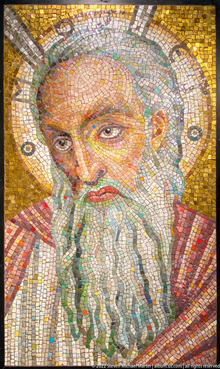 A bearded man’s face and shoulders are rendered in small colored mosaic tiles against gold.