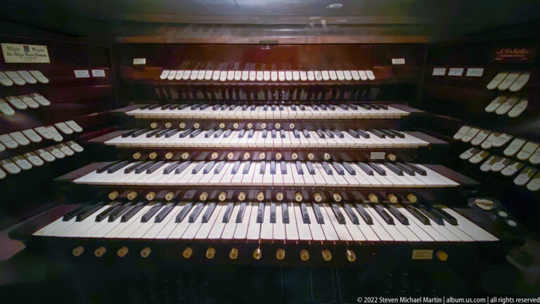 A dark pipe organ console has several stacked keyboards and rows of stop controls.