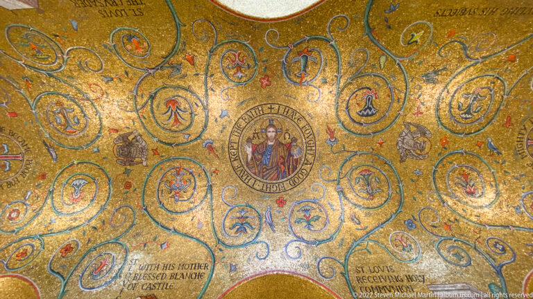 A haloed figure in a round medallion is surrounded by smaller mosaics and ornament on a gold ceiling.