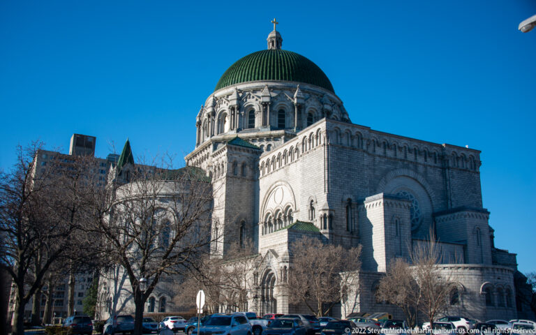 The cathedral’s green dome rises above pale stone apses and arched windows, partly screened by bare trees.