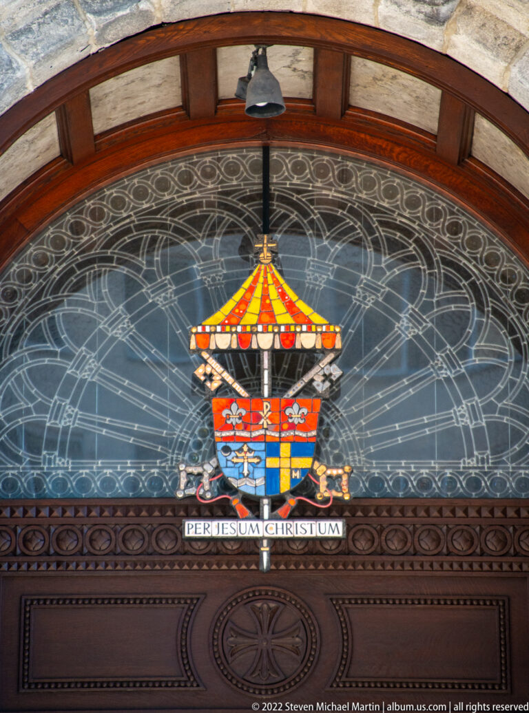 A circular floor medallion displays a multicolored shield and the Latin phrase “Per Jesum Christum.”