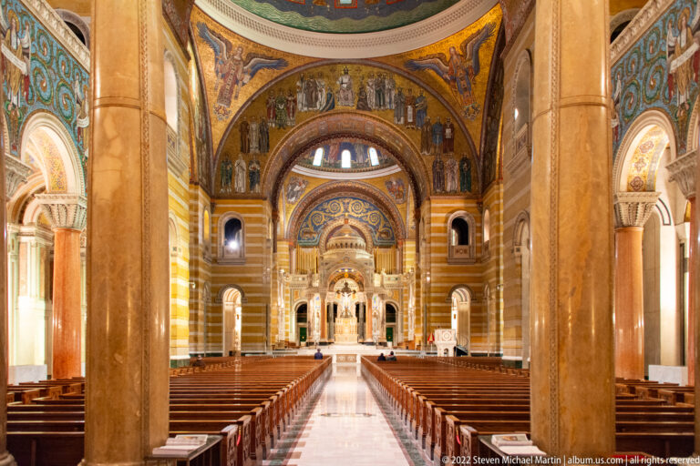 Rows of pews and a central aisle lead toward the altar beneath decorated arches and massive marble columns.