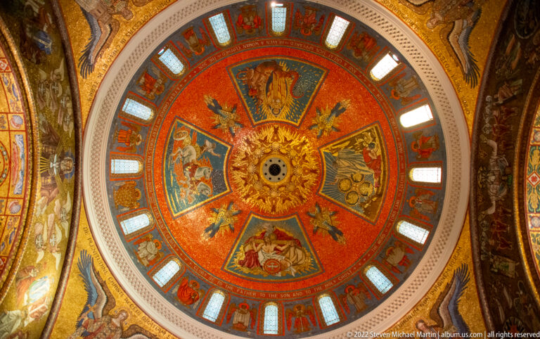 A circular cathedral dome displays orange-and-gold mosaic panels around a central medallion, with windows around its base.