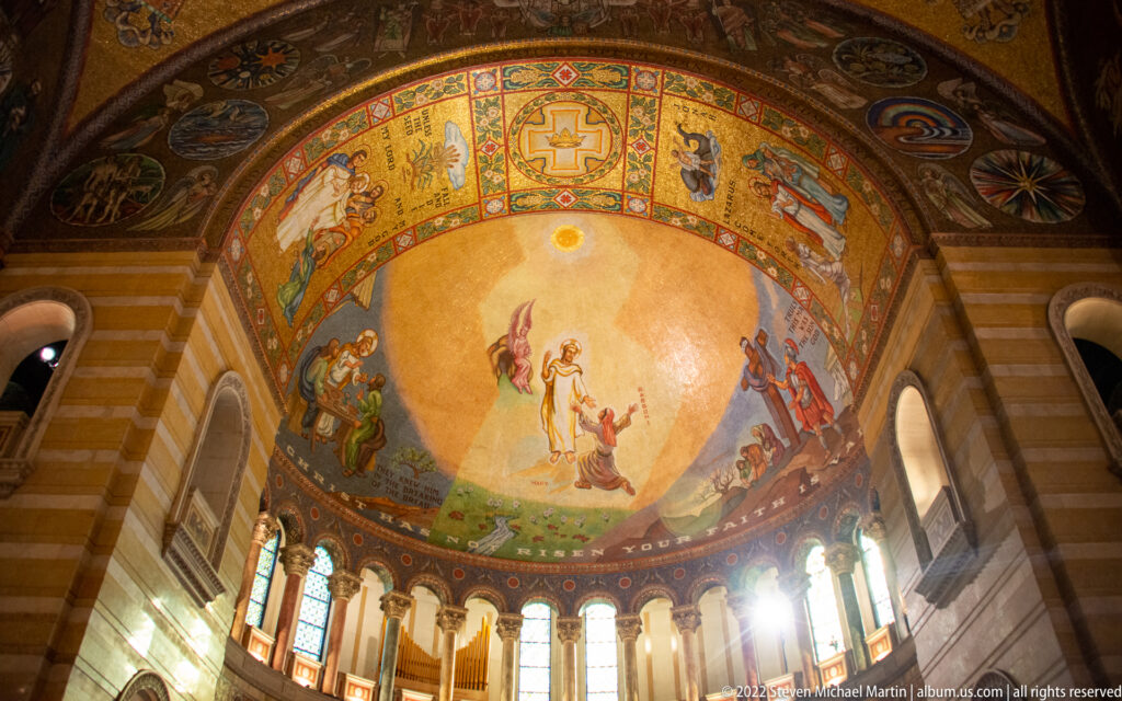 A cathedral apse mosaic shows a baptism scene above tall windows, surrounded by smaller biblical figures and decorative bands.