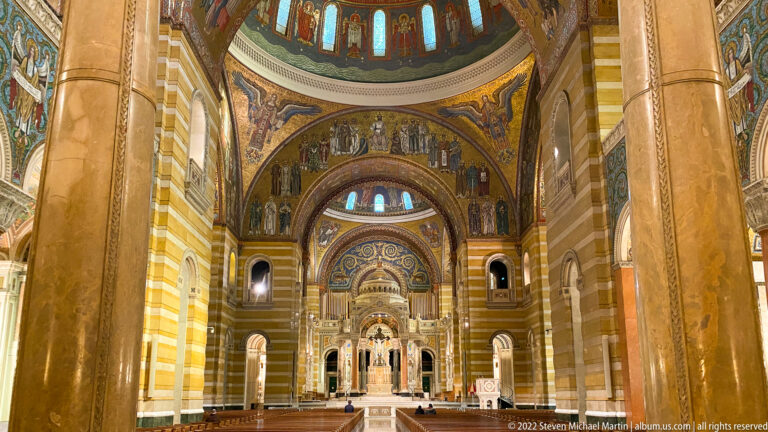Banded marble piers frame the nave and mosaic-covered sanctuary beneath colored upper windows.