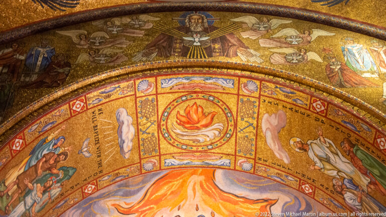 A mosaic band with a central dove-like emblem and angels sits above an orange apse scene and flame medallion.