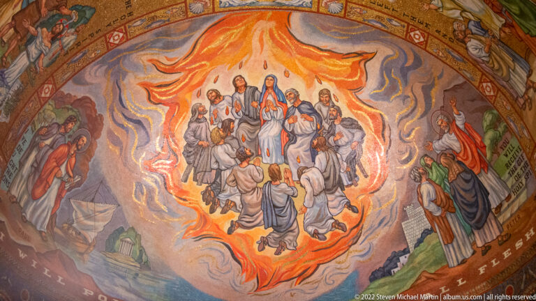 A group of figures gathers inside a flame-shaped orange field, with worshippers below and gold lettering along the border.