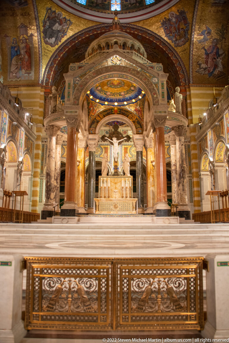 A marble altar sits beneath mosaic arches behind an ornate metal communion rail and paired columns.