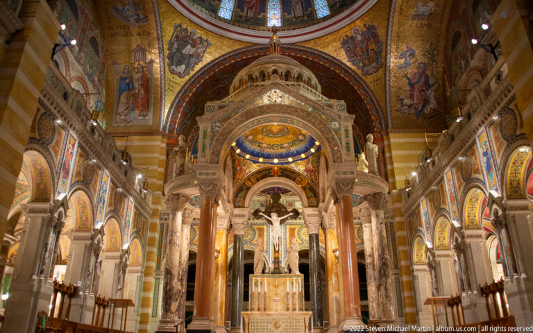A wide interior view looks through the cathedral toward the altar beneath mosaics, arches, columns, and a distant dome.