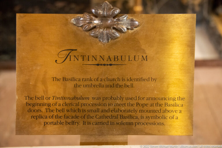 A brass label explains the tintinnabulum bell and its role as a symbol of basilica status and processions.