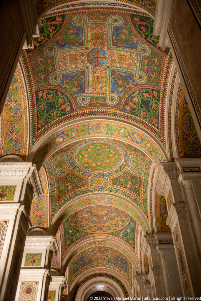 Geometric and floral mosaics fill the cathedral’s vaulted ceiling between pale stone ribs and repeated arches.