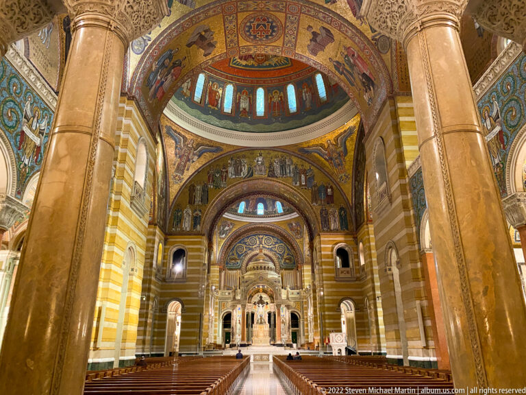 Rows of pews flank the central aisle beneath mosaic arches and lead toward the cathedral altar.