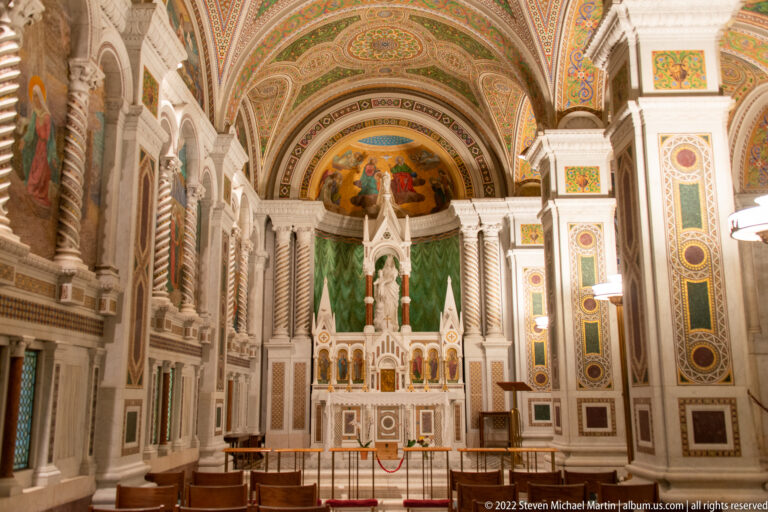 A side altar with a central statue, green drapery, candles, and a small apse mosaic stands behind a low barrier.