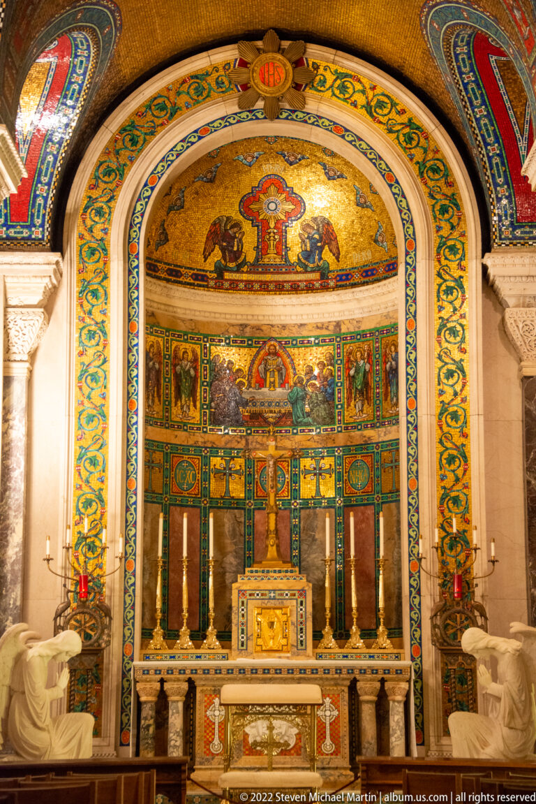 The central altar sits beneath a gold and multicolored mosaic apse, framed by columns and flanked by kneeling white sculptures.