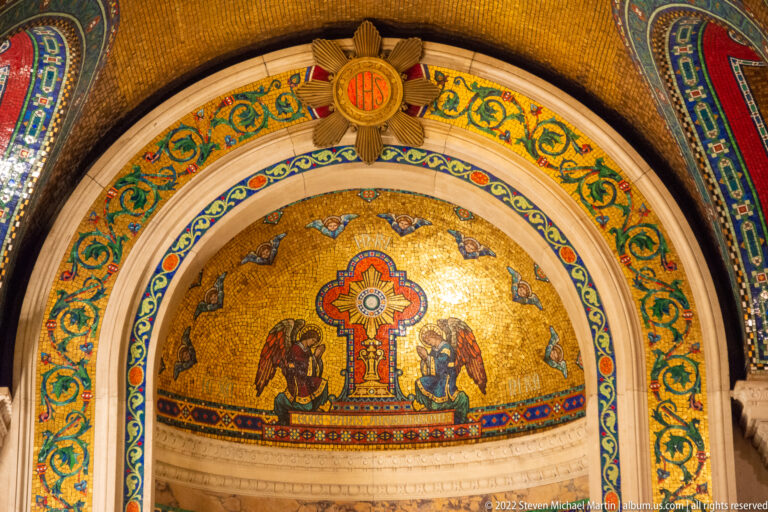 A gold mosaic lunette shows a central cross between two kneeling blue-winged angels, inside nested ornamental arches.