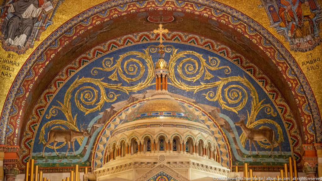 Two deer flank a small domed building in a blue-and-gold apse mosaic above an architectural half-dome.
