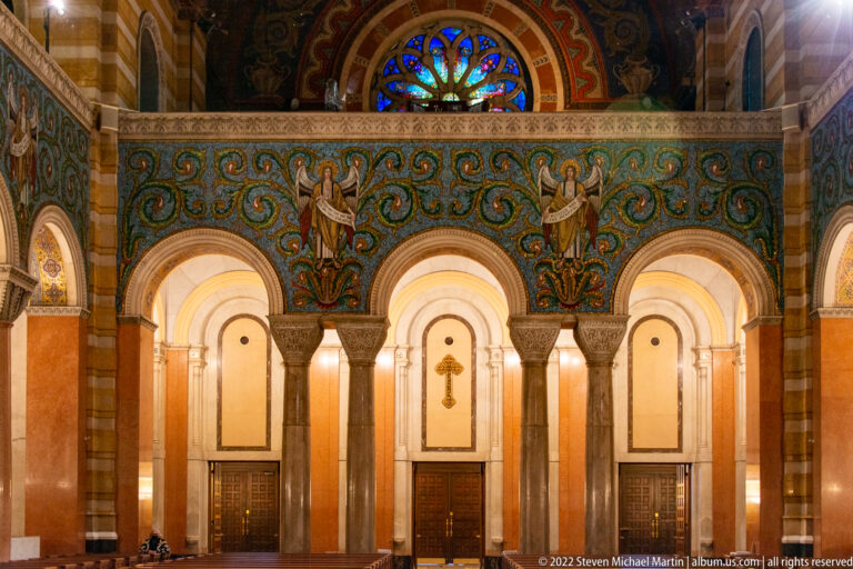 Two standing figures appear in a blue-green mosaic frieze above three bright arches, with part of a rose window above.