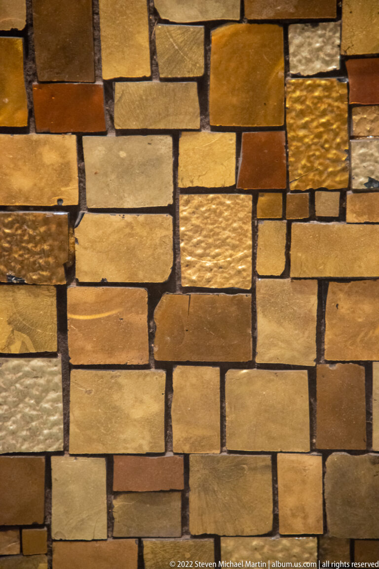 Large gold, ochre, and brown rectangular tesserae sit in staggered rows, with varied textures and dark joints.