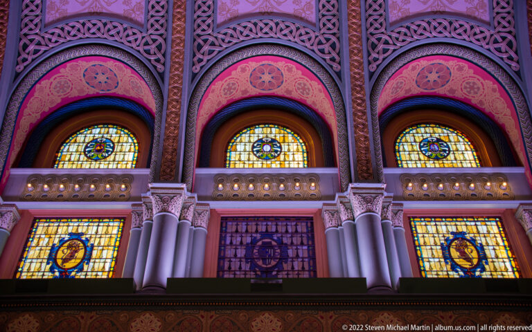 Three stained-glass windows fill decorated arches above a row of smaller panels.