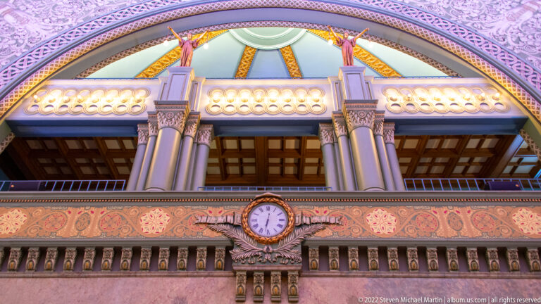 A clock and carved frieze sit below an upper gallery with stained-glass windows.