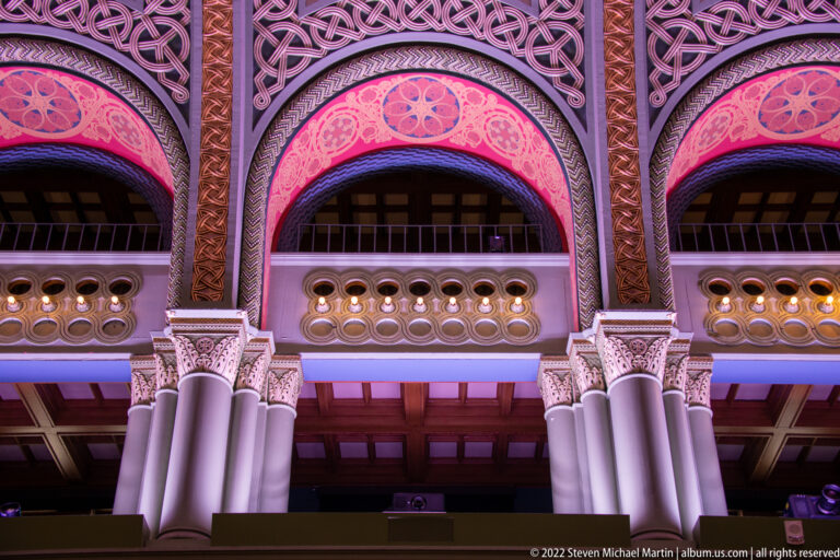 Three pink-lit arches with interlaced ornament rise above a balustrade in the Grand Hall.