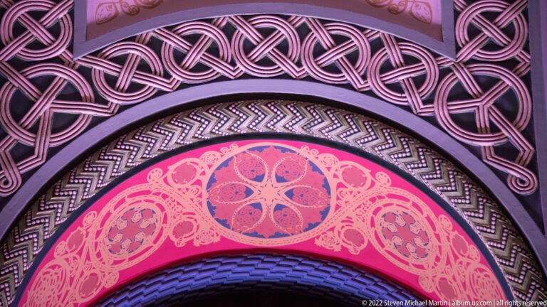 A curved pink-lit arch contains interwoven bands and a central circular ornament.