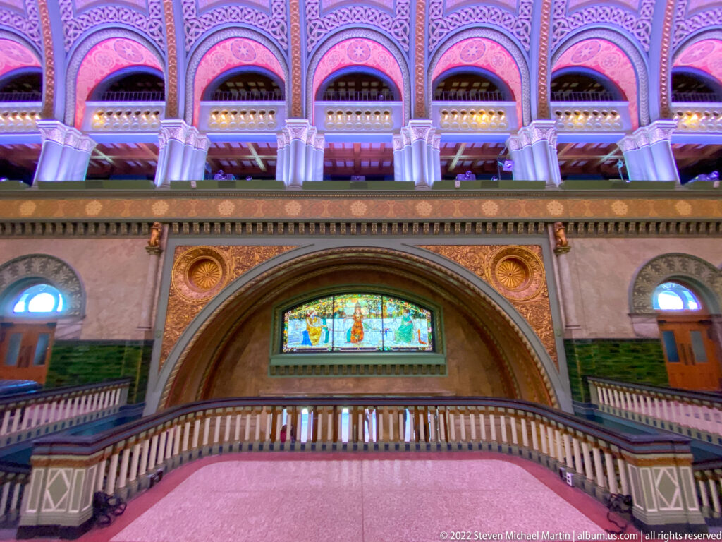 A stained-glass panel sits above a balcony beneath a large decorated arch.