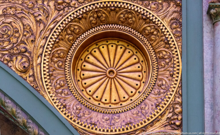 A carved circular ceiling rosette has radiating spokes and concentric bands of figures and foliage.