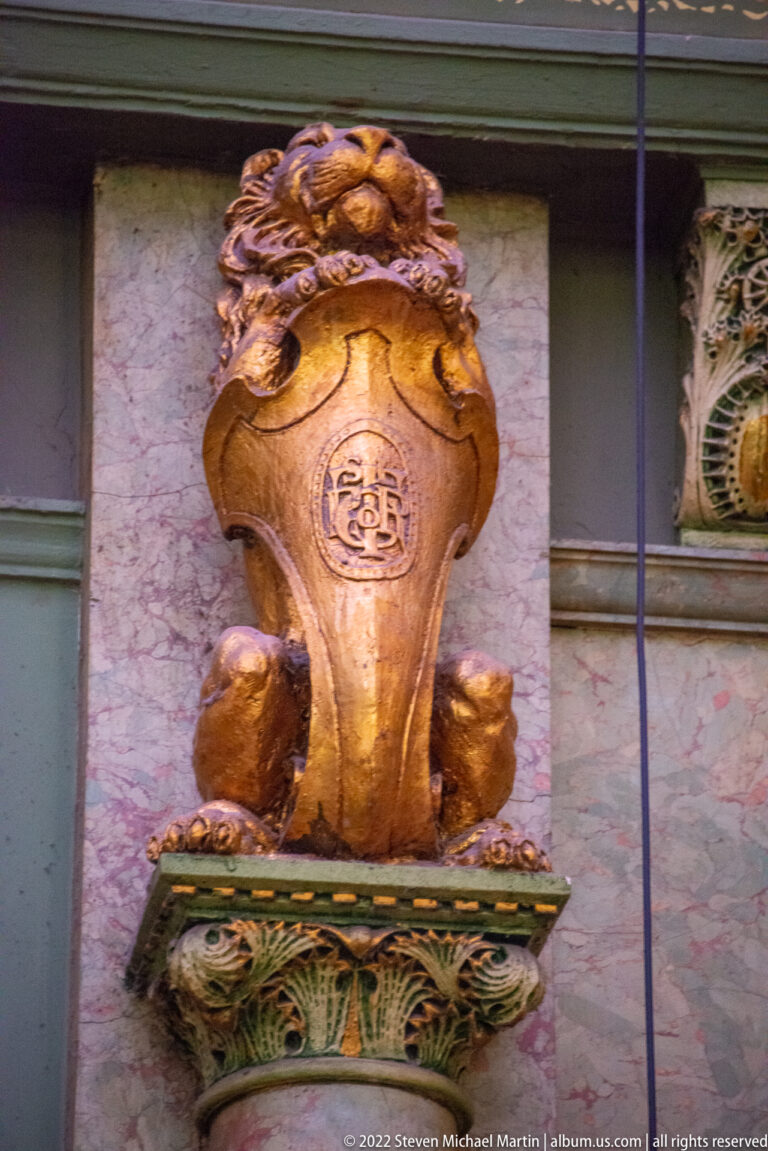 A gold-toned sculptural wall feature with an oval medallion projects above a green ornamental base.