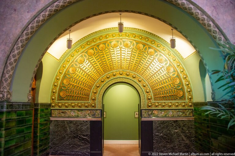 A large gilded fan-shaped relief crowns an arched doorway set in deep green-tiled walls.