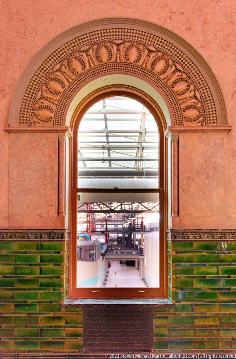 An arched opening with patterned trim and green tile looks through to the steel train shed.