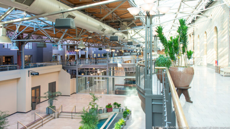 A glass-roofed atrium contains balconies, walkways, palms, and a “Hotel Lobby” sign.