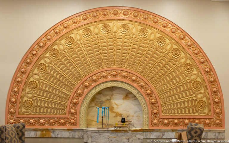 A gilded semicircular relief with radiating shell forms rises above a marble ledge.