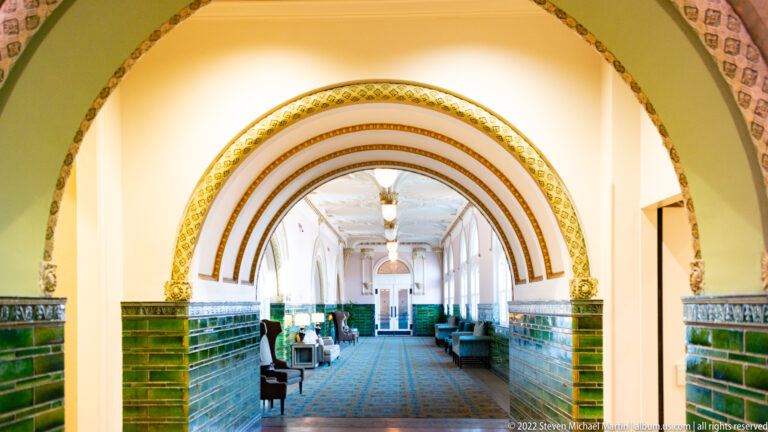 Nested arches frame a long green-tiled passage with chairs and tables along both sides.