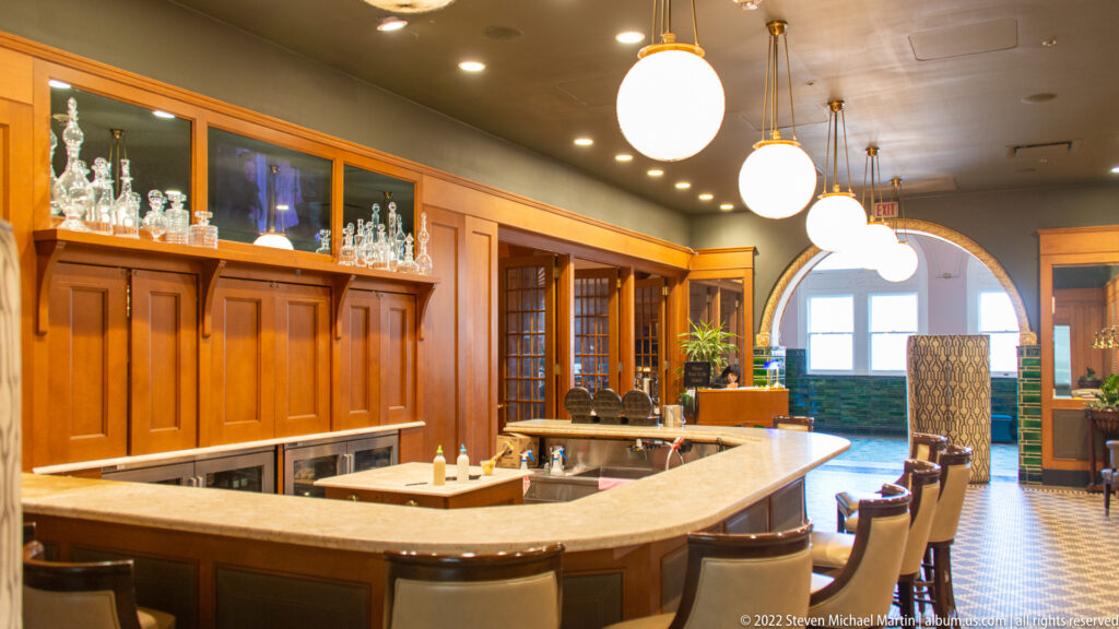 A curved bar with stools sits beneath globe pendants in a wood-paneled room.