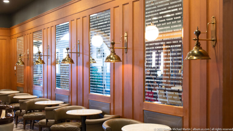 Brass bells hang above café tables beside wood panels and dark lettered plaques.
