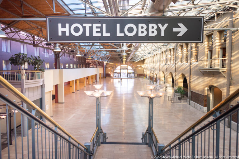 A large HOTEL LOBBY arrow hangs above a bright corridor with glass roofing and stair rails.