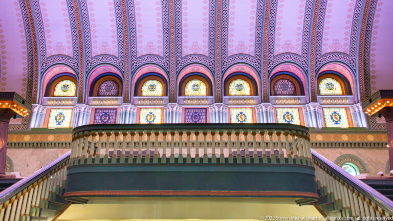Colorful arched stained-glass windows and patterned ornament rise above the Grand Hall balcony.