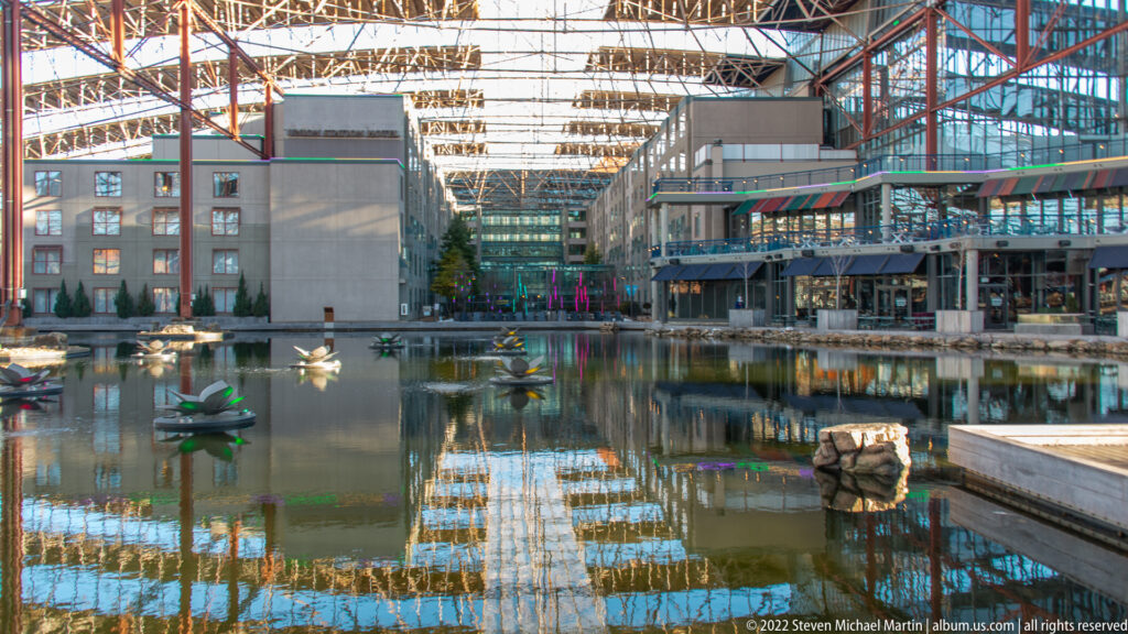 A reflecting pool mirrors the glass roof and storefronts of a covered retail arcade.
