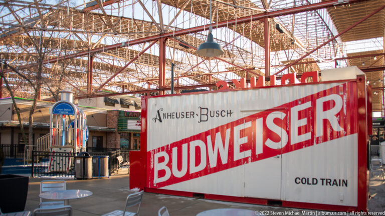 A white railcar marked BUDWEISER and COLD TRAIN stands beneath a glass-and-steel roof.