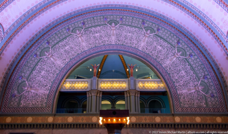 A decorated arch frames an upper balcony with columns and small lights.
