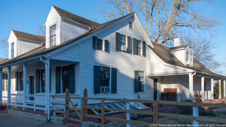 The Louis Bolduc House has a long clapboard side, green shutters, and a raised gallery.