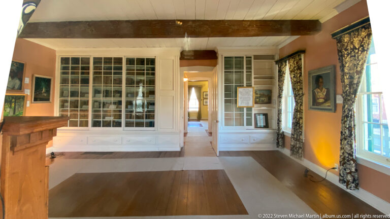 Glass-front cabinets line a historic room around a central doorway, with a counter and portrait nearby.