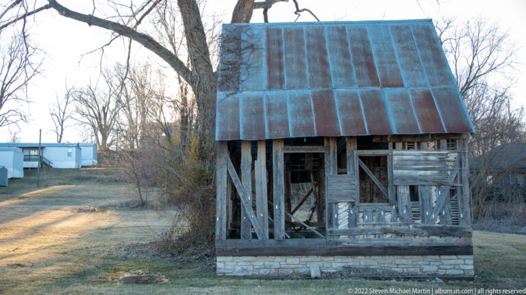 An open timber frame rises above a low stone base beneath a steep metal roof.