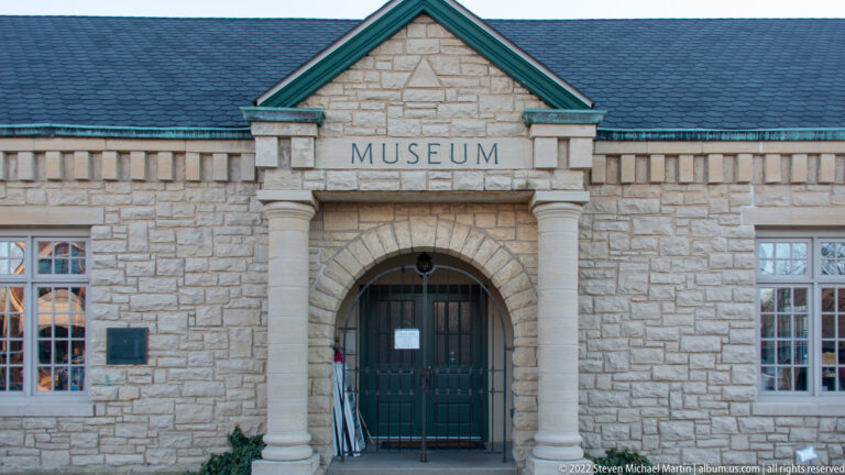 The word MUSEUM is carved above an arched entrance flanked by columns in a pale stone façade.