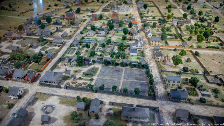 A scale model shows blocks of miniature houses, gardens, trees, and a broad central street.
